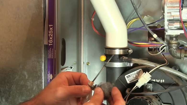 Hands cleaning a furnace's flame sensor with a super fine steel wool