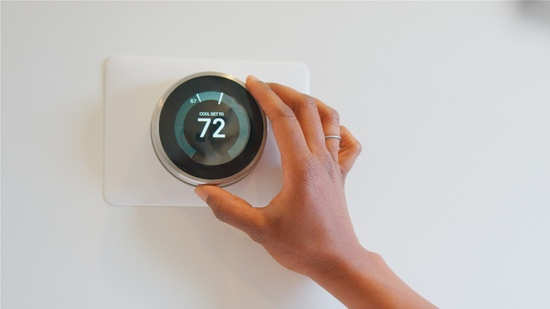 Someone adjusting the temperature on a thermostat attached to the wall