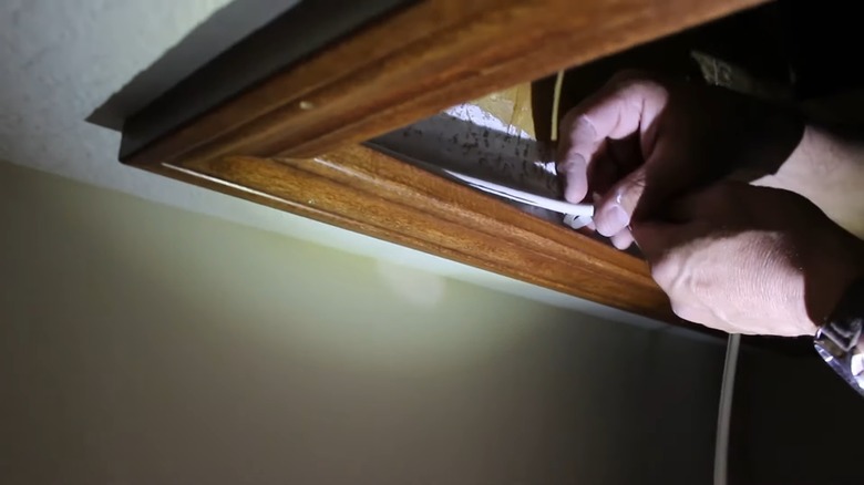 A close up of someone's hands adding weather stripping to the corners of an attic hatch