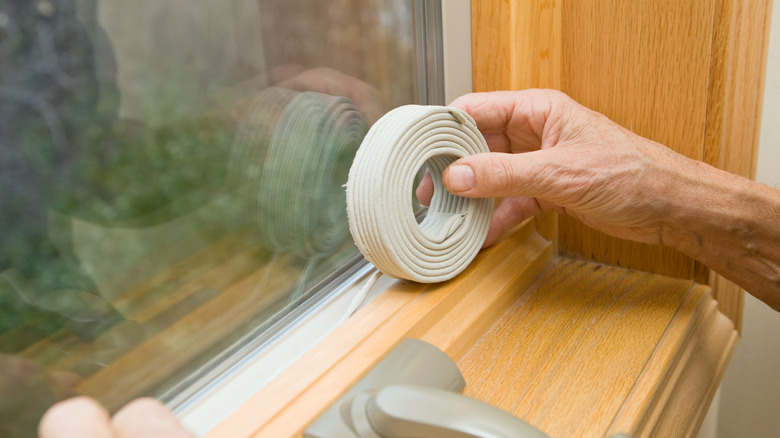 Hands weatherstripping a drafty window