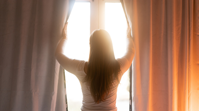 Woman opening thick curtains to let in sunlight