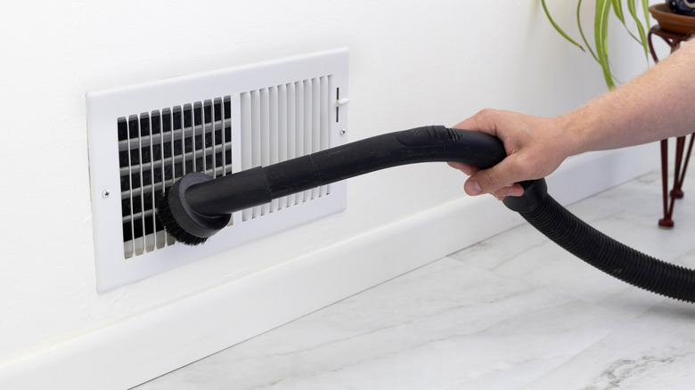 Someone hand vacuuming an air vent close to the floor