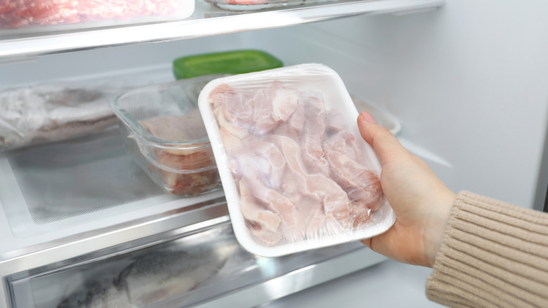 A person taking a package of chicken out of fridge