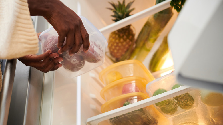 A person organizing containers on a refrigerator shelf