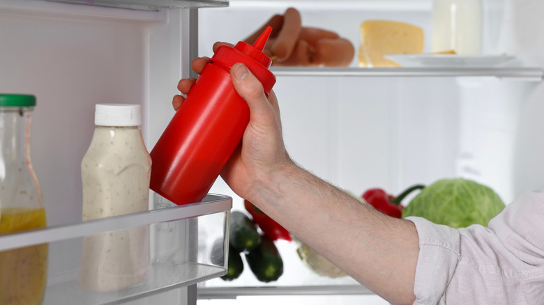 A person taking ketchup out of refrigerator