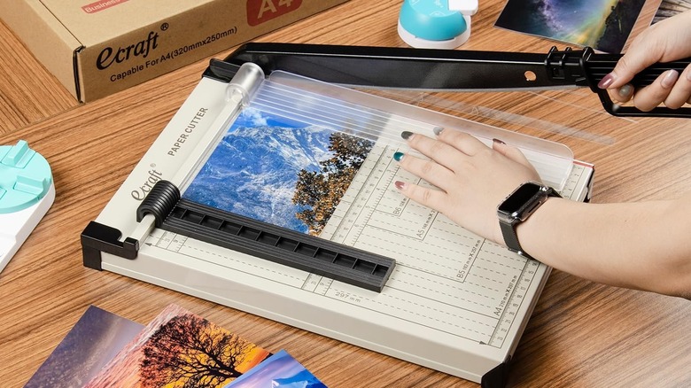 Woman using paper cutter to crop photo
