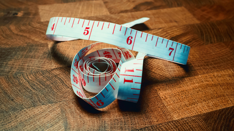 White, flexible measuring tape with red lettering on a checkered wood table