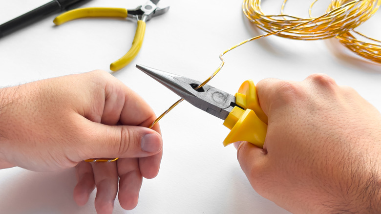 Two hands using needle nose pliers to cut yellow crafting wire