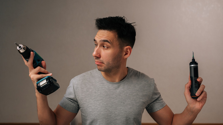 man holding full-sized and pocket-sized electric screwdrivers