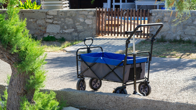 A blue collapsible wagon sits on a gravel path in a backyard