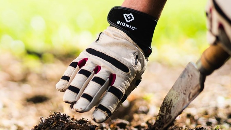 A person wearing Bionic ReliefGrip Gardening Gloves uses a trowel in the dirt