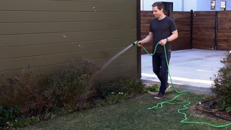 A man uses a green flexible hose to water a garden bed