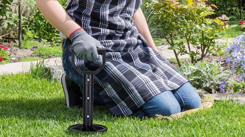A woman wearing a checked apron holds a black mobility aid tool while kneeling in the garden