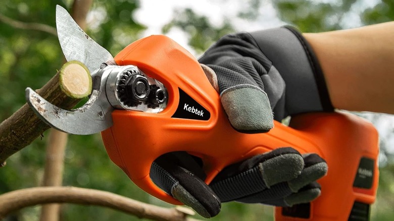A person uses an orange Kebtek Cordless Portable Electric Pruner to cut a branch