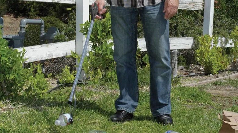 A man uses an EZ Reach & Grab Reaching Tool to pick up trash from a lawn