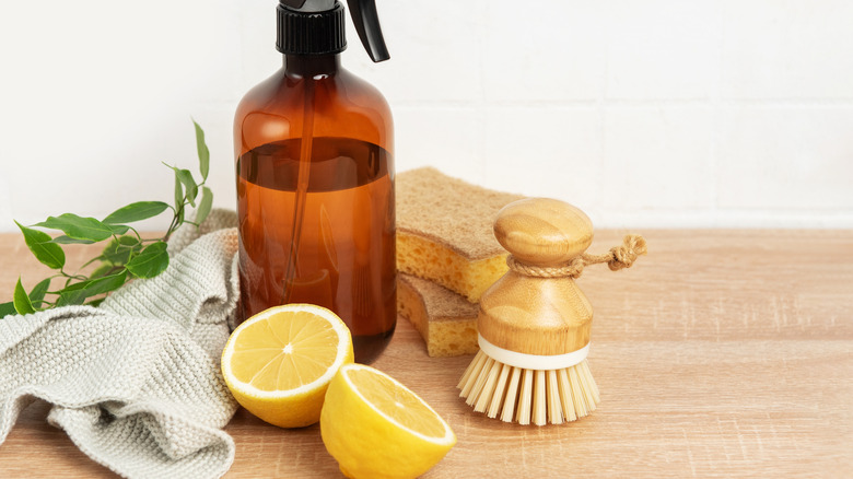 A spray bottle with lemon and a scrubbing brush on a wooden table