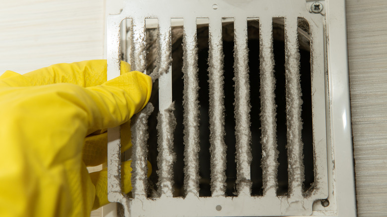 Gloved hand holds dusty air vent cover.