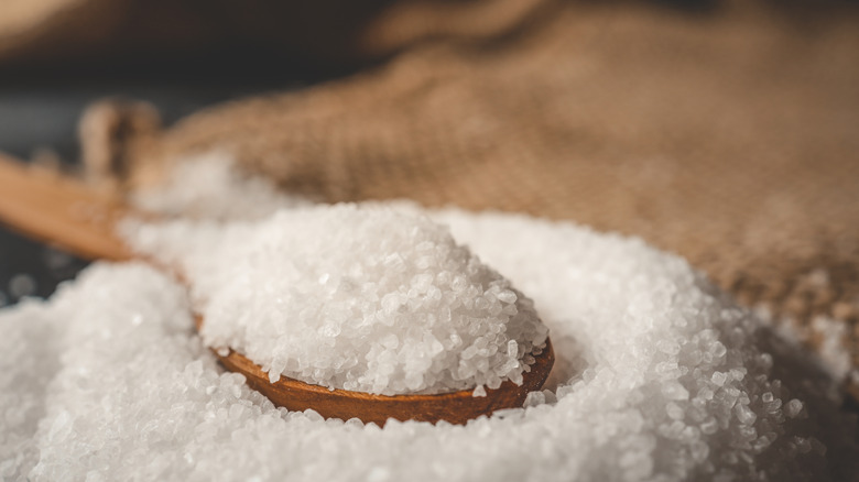 Grains of salt on a wooden table with a wooden spoon