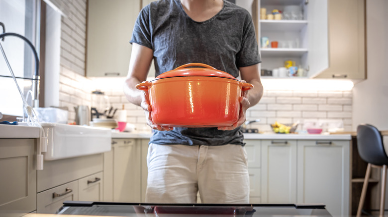 Someone holding an orange Dutch oven before putting it in the oven