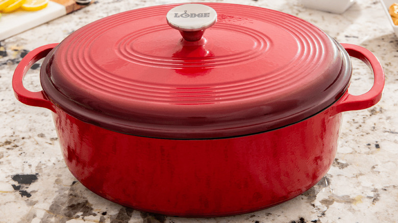 A red Dutch oven sitting on a countertop with its lid on