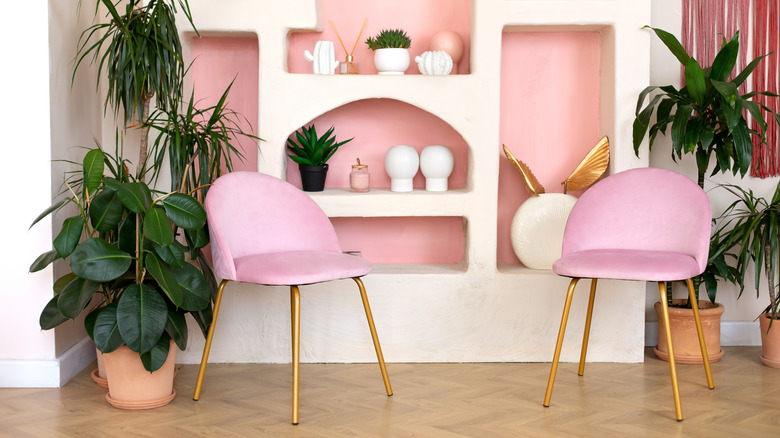 A Memphis Design space with two curvy pink chairs against a pastel pink and white wall with decor on the shelves