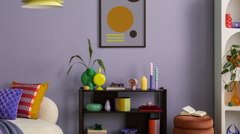 An 80s-inspired living room with a purple wall and neon green and yellow vases on a black bookshelf