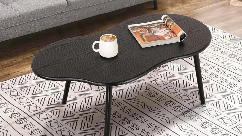A black asymmetrical coffee table sits in a living room with a mug and book on it
