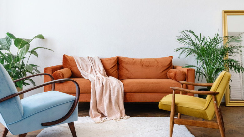 A living room with a white wall and a rusty brown sofa, a blue chair, and a yellow chair
