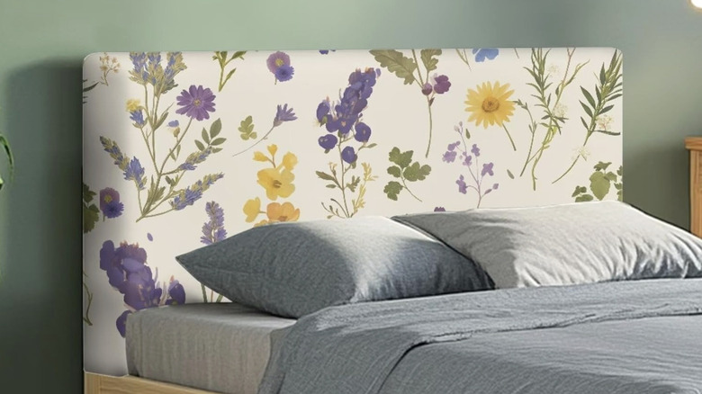 A platform bed with a floral headboard cover and gray sheets and pillow cases