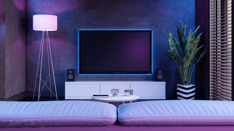 A living room lit by blue and purple lights with a TV outlined in blue neon lights above a white console