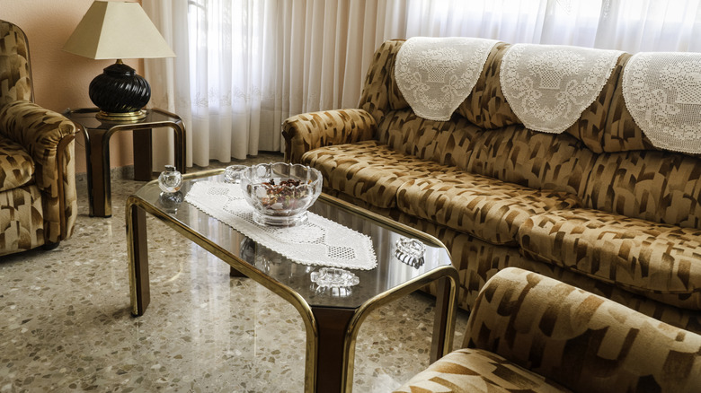 A living room styled with pastel pink walls, oversized couch and chair, and a glass coffee table with high-shine brass trim
