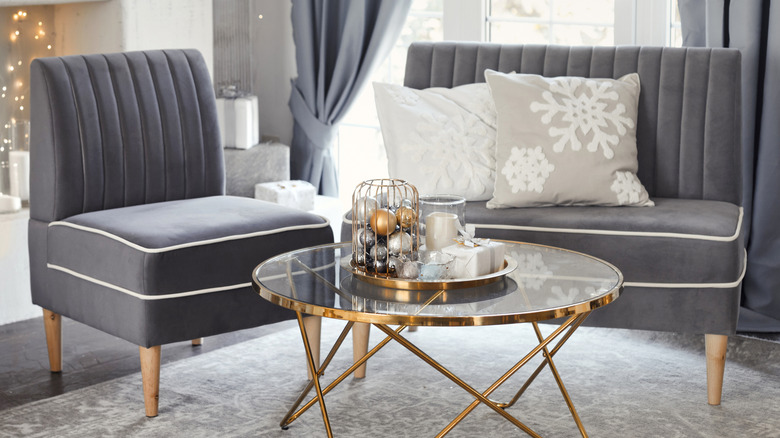 A living space with a seate and chair in gray with a glass-topped coffee table with a brass finish