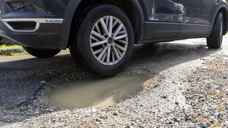 Close-up of a car wheel next to a gravel pothole