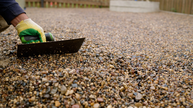 A construction working carefully spreading resin-bound aggregate on a driveway