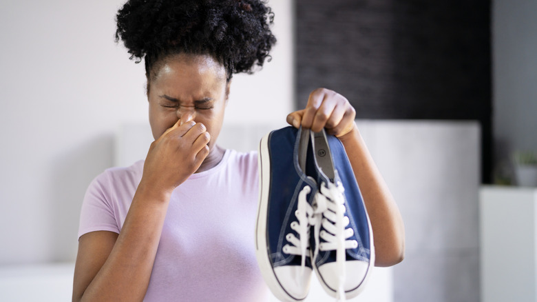 A person plugging their nose and holding up a pair of smelly tennis shoes
