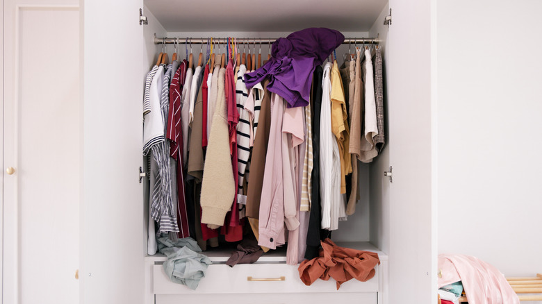 A messy closet with clothes hanging and draped out of drawers