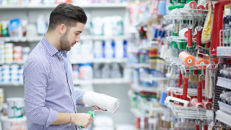 A person holding a paint roller looks at the options in a hardware store.