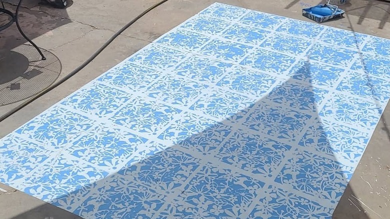 A blue and white stenciled faux rug on a concrete slab patio.