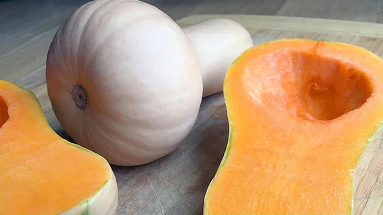 One whole and one cut in half 'Burpee Butterbush' squash on a cutting board