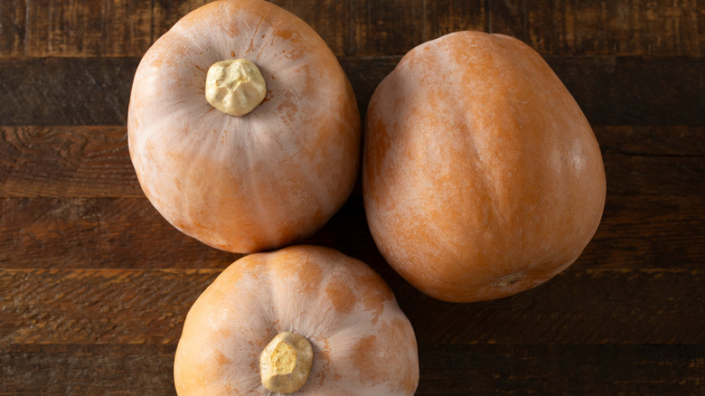 A top-down view of three orange 'Honeynut' squash on a wooden surface