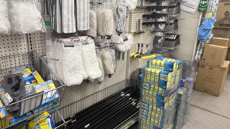 Dollar store broomsticks, mops, and handles hanging in a store aisle