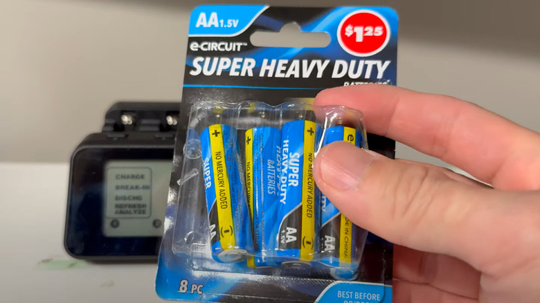 Man holding open package of dollar store AA batteries in front of testing device