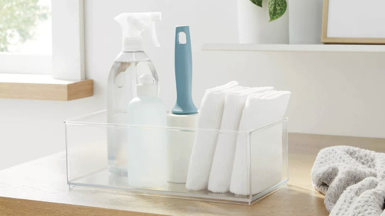 A clear storage bin holding cleaning supplies and laundry products