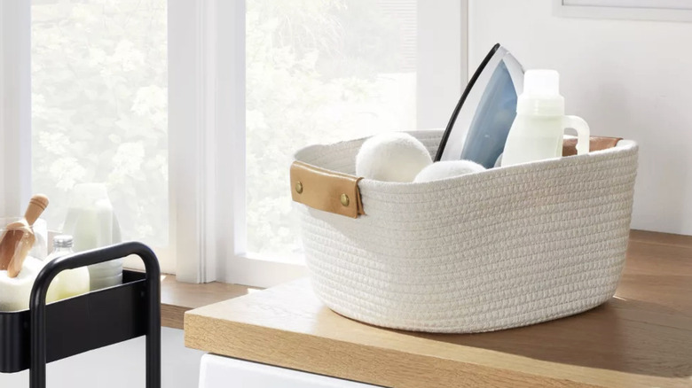 A white woven basket holding dryer balls, an iron, and laundry detergent