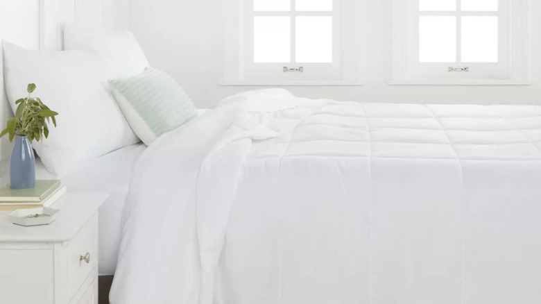 A bed with white bedding and a light green throw pillow