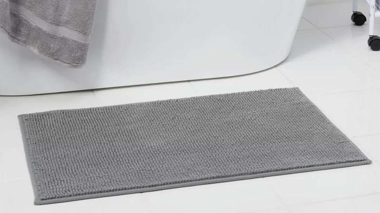 A gray chenille bath rug in front of a bathtub