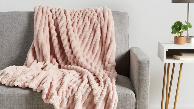 A fuzzy pink throw blanket draped over a gray couch