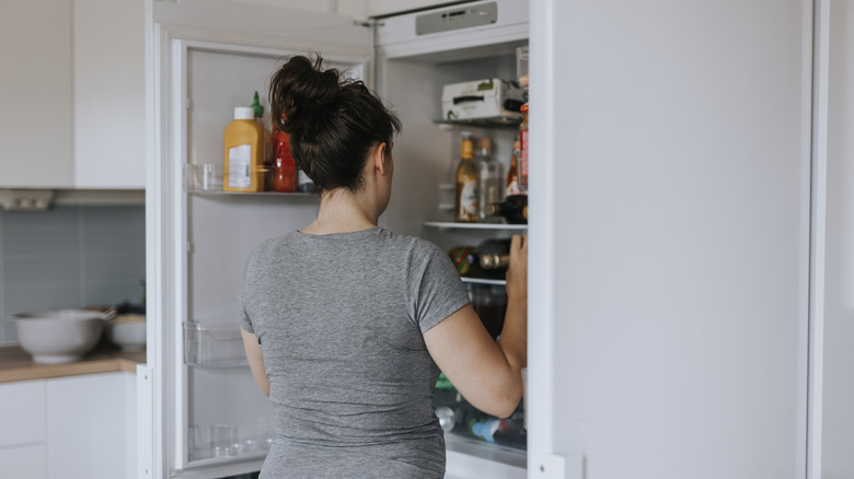 Woman standing in front of cluttered fridge.