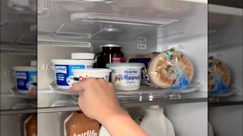 Person spins plastic turnable in fridge with items on top.
