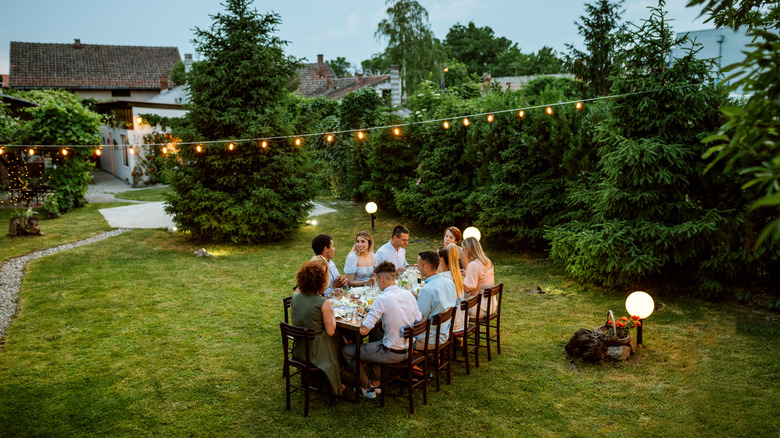 A group of friends gathered around a table in the middle of a well-kept, flourishing garden